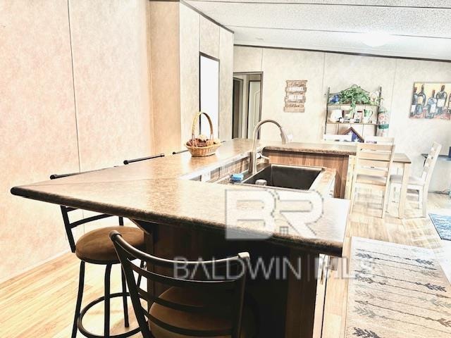 kitchen with light hardwood / wood-style flooring, sink, a textured ceiling, light stone counters, and a breakfast bar