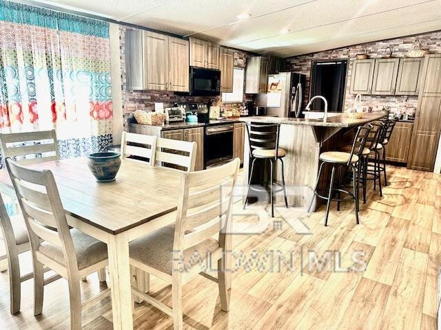 kitchen with light hardwood / wood-style flooring, sink, fridge, stainless steel electric range oven, and a breakfast bar