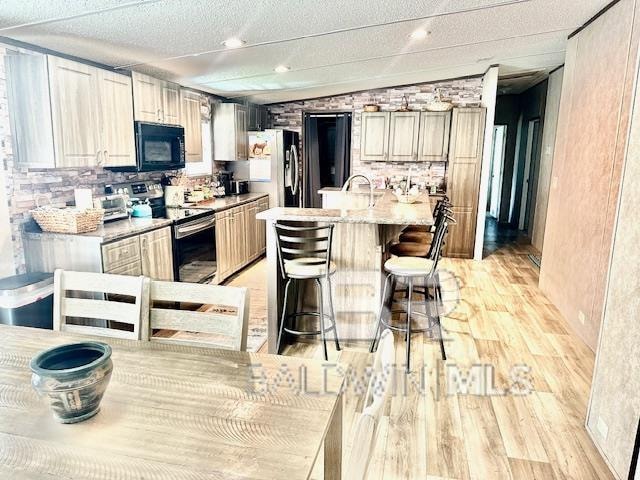 kitchen featuring a kitchen island with sink, a kitchen breakfast bar, light hardwood / wood-style flooring, appliances with stainless steel finishes, and light stone counters