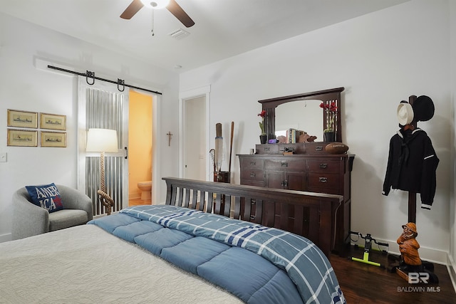 bedroom featuring dark hardwood / wood-style flooring, a barn door, ceiling fan, and ensuite bathroom