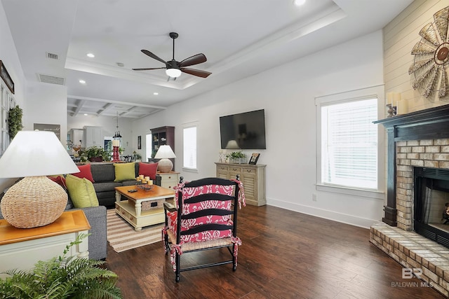 living room with dark hardwood / wood-style flooring, a brick fireplace, and a tray ceiling