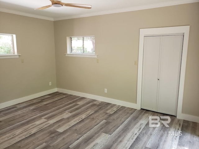 unfurnished bedroom featuring ornamental molding, multiple windows, wood-type flooring, and ceiling fan