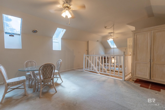 interior space featuring vaulted ceiling with skylight, carpet floors, ceiling fan, and baseboards