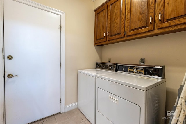 laundry area featuring washing machine and clothes dryer, light tile patterned flooring, baseboards, and cabinet space