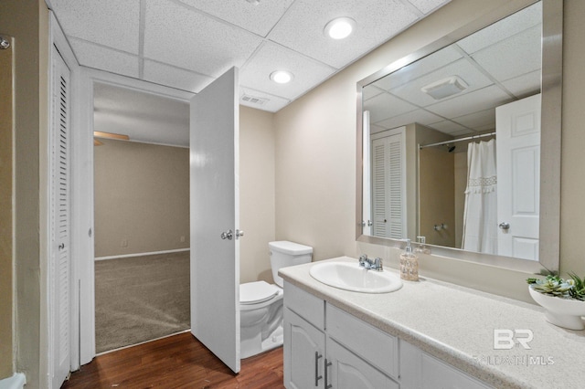 bathroom featuring wood-type flooring, vanity, toilet, and a drop ceiling