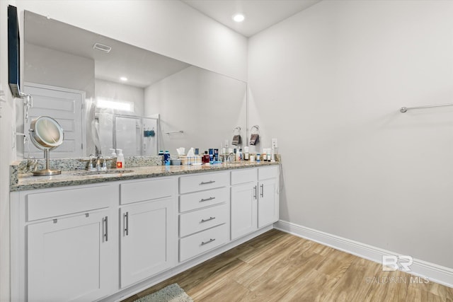 full bath featuring double vanity, a sink, a shower stall, and wood finished floors