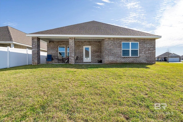 rear view of property featuring brick siding, roof with shingles, fence, and a yard