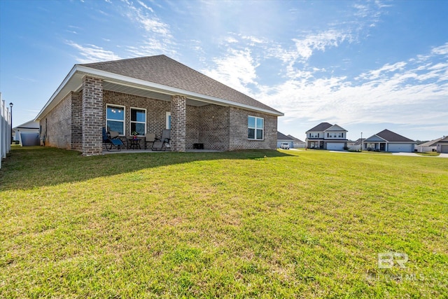 rear view of house with brick siding, a shingled roof, a patio area, and a yard