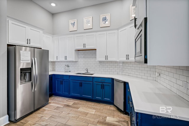 kitchen featuring light countertops, white cabinets, a sink, blue cabinets, and stainless steel fridge