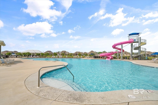 community pool featuring a water slide, a patio area, and fence