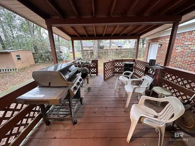 wooden deck featuring an outbuilding, grilling area, a storage shed, and fence