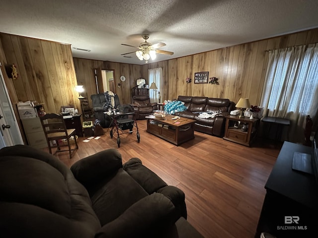 living room with wooden walls, wood finished floors, visible vents, ceiling fan, and a textured ceiling