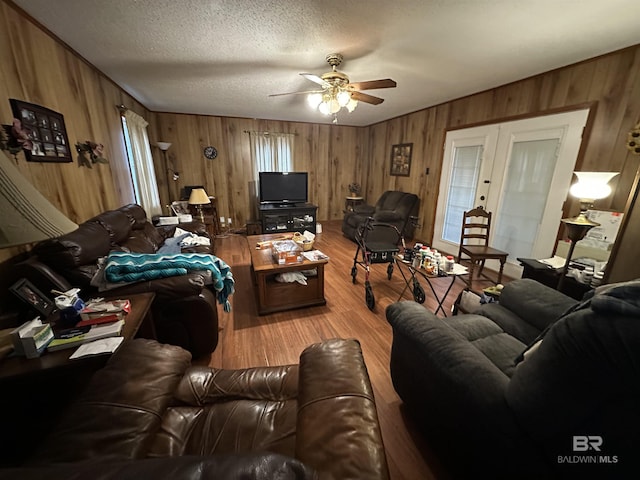 living area with wood finished floors, a textured ceiling, ceiling fan, and wood walls