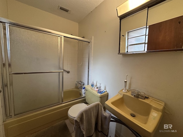 full bath featuring visible vents, toilet, a sink, a textured ceiling, and bath / shower combo with glass door