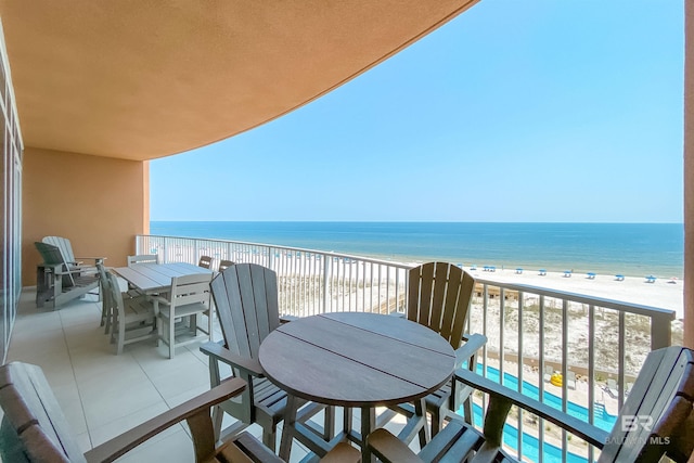 balcony featuring outdoor dining area, a water view, and a view of the beach