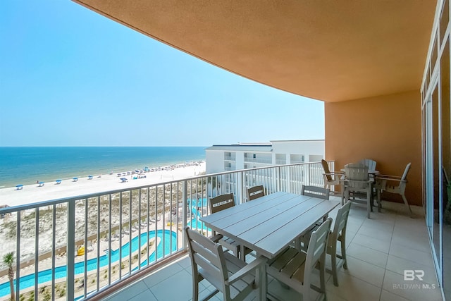 balcony with outdoor dining space, a water view, and a view of the beach