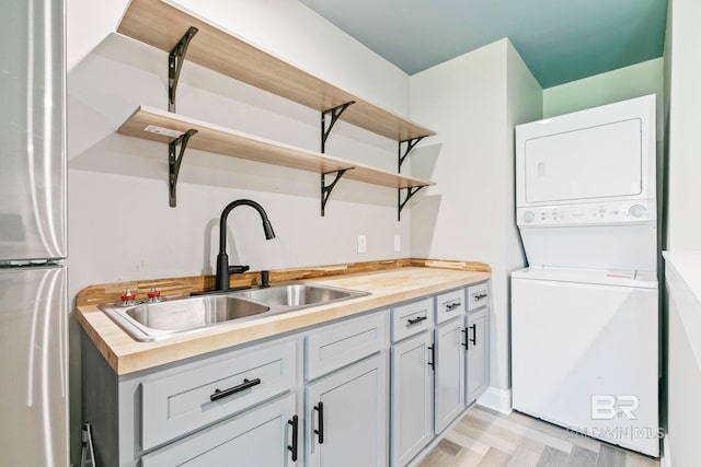 kitchen featuring wood counters, sink, stacked washer and clothes dryer, and stainless steel refrigerator