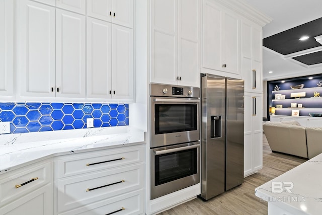 kitchen with light stone countertops, stainless steel appliances, white cabinets, and light wood-type flooring