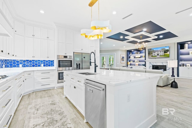 kitchen featuring white cabinetry, sink, hanging light fixtures, stainless steel appliances, and a center island with sink