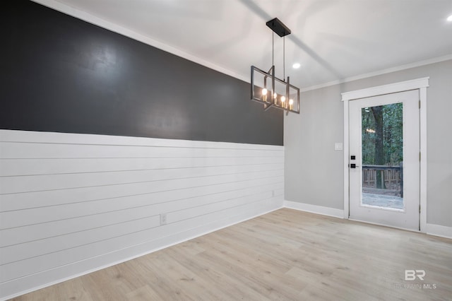 unfurnished dining area featuring crown molding, a notable chandelier, light hardwood / wood-style floors, and wood walls