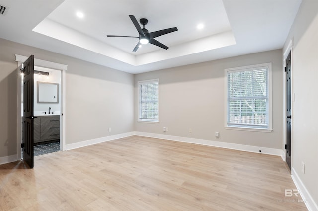 unfurnished bedroom featuring a raised ceiling, multiple windows, and light hardwood / wood-style floors