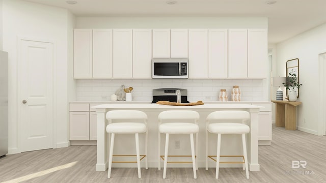 kitchen featuring stainless steel microwave, backsplash, light countertops, range, and light wood-style floors