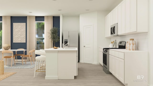 kitchen featuring light wood-style flooring, a kitchen bar, an island with sink, light countertops, and appliances with stainless steel finishes