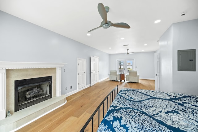 bedroom with french doors, light hardwood / wood-style floors, electric panel, ceiling fan, and a premium fireplace