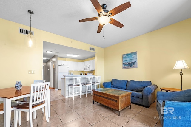 living room featuring a textured ceiling, light tile patterned floors, and ceiling fan