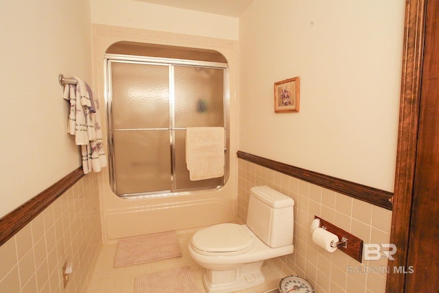 bathroom with tile walls, tile patterned floors, toilet, and shower / bath combination with glass door