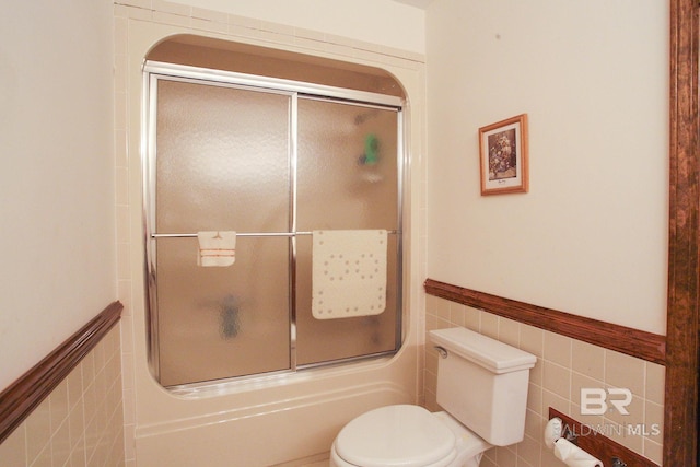 bathroom with toilet, combined bath / shower with glass door, and tile walls