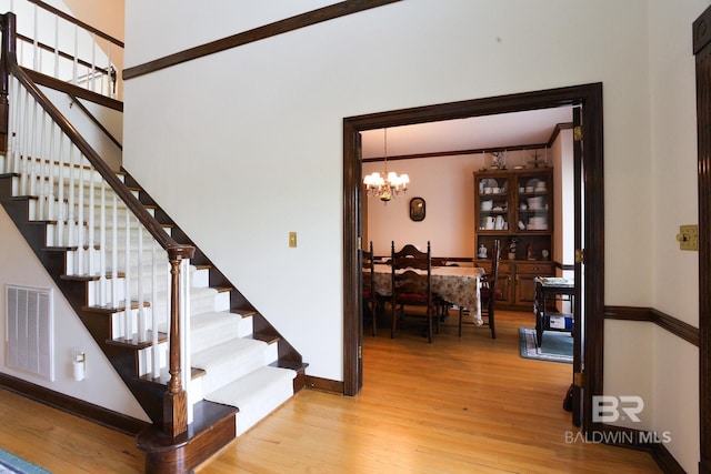 staircase featuring crown molding, light hardwood / wood-style flooring, and a notable chandelier