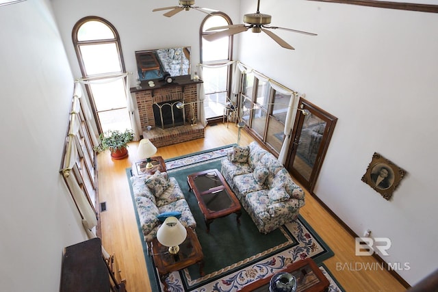 living room featuring a fireplace, wood-type flooring, ceiling fan, and a towering ceiling