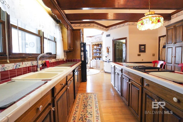 kitchen with tile counters, light hardwood / wood-style flooring, hanging light fixtures, and sink