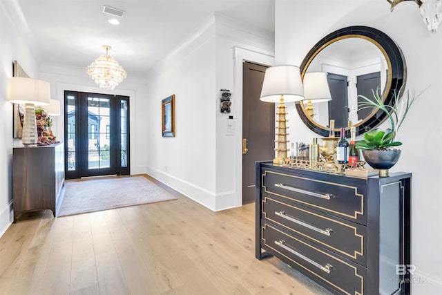 foyer entrance with ornamental molding, light hardwood / wood-style flooring, and an inviting chandelier