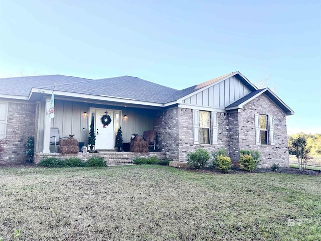 ranch-style home featuring brick siding, board and batten siding, a front yard, and a shingled roof