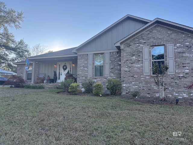 ranch-style home with board and batten siding, a front yard, brick siding, and a porch