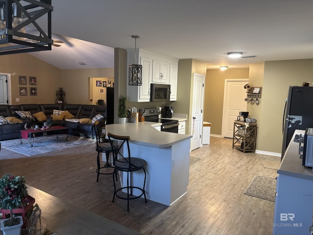 kitchen featuring lofted ceiling, white cabinets, appliances with stainless steel finishes, light hardwood / wood-style floors, and a breakfast bar area