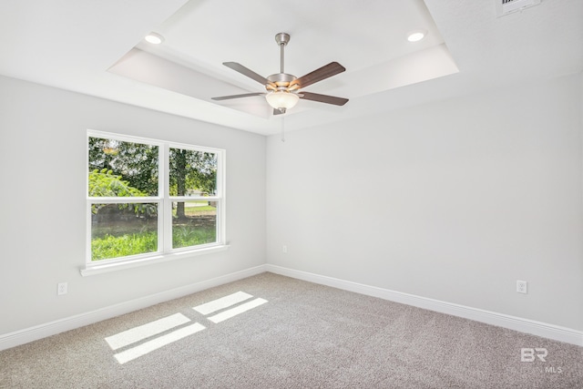 empty room with a tray ceiling, ceiling fan, and carpet