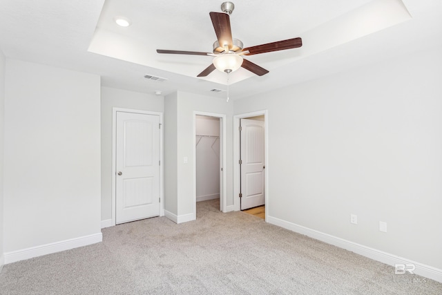 unfurnished bedroom with light carpet, a tray ceiling, ceiling fan, a spacious closet, and a closet