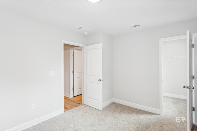 unfurnished bedroom with a walk in closet, light carpet, and a closet