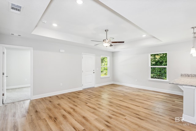 unfurnished living room with ceiling fan, light wood-type flooring, and a tray ceiling