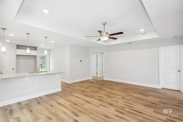 unfurnished living room with light wood-type flooring, a raised ceiling, ceiling fan, and sink