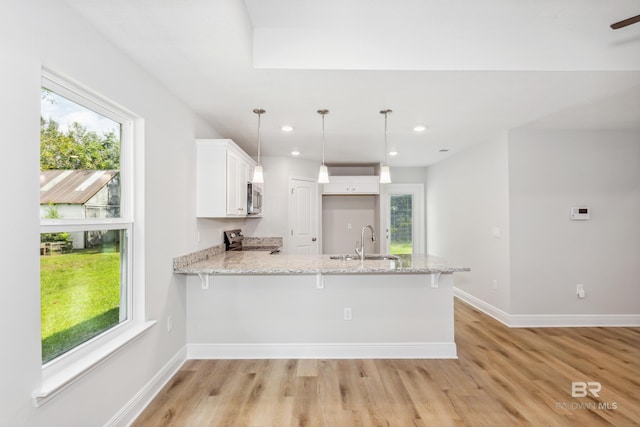 kitchen with sink, kitchen peninsula, decorative light fixtures, light hardwood / wood-style floors, and white cabinetry