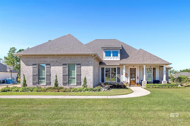 view of front of property featuring a front yard, roof with shingles, covered porch, and brick siding
