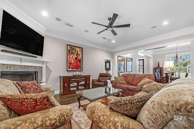 living room featuring wood finished floors, ceiling fan with notable chandelier, a brick fireplace, visible vents, and crown molding