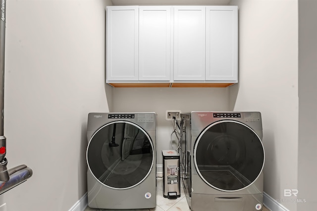 laundry area featuring light tile patterned flooring, washer and clothes dryer, cabinet space, and baseboards