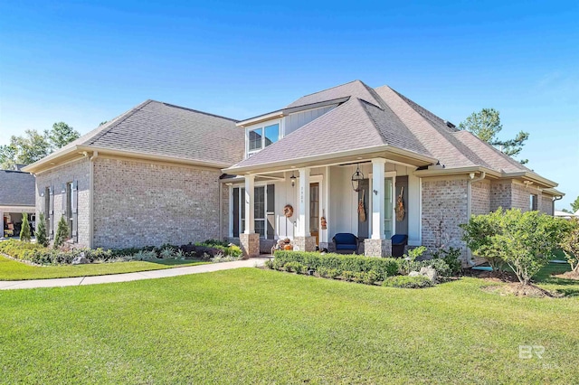 view of front of property featuring a front lawn, a porch, a shingled roof, and brick siding