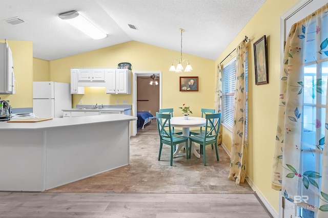 kitchen with light hardwood / wood-style flooring, white refrigerator, decorative light fixtures, vaulted ceiling, and white cabinets