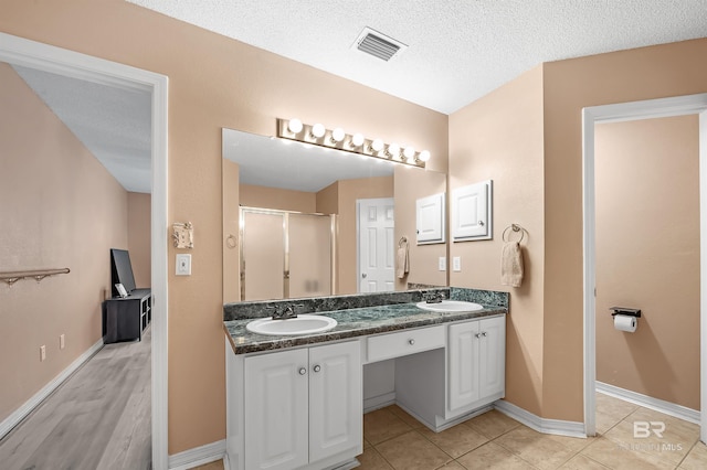 bathroom with tile patterned flooring, vanity, a textured ceiling, and walk in shower